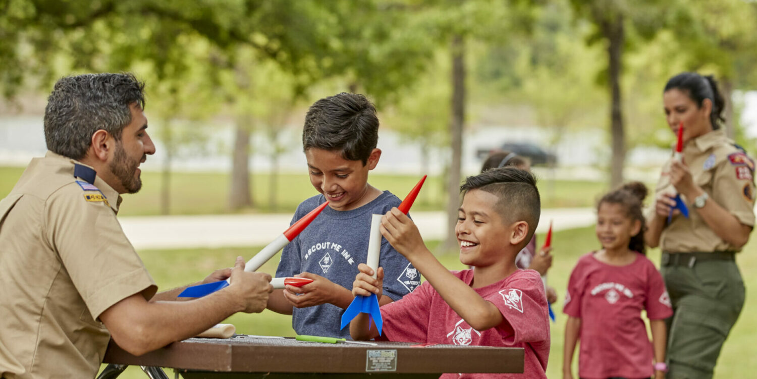 A group of Cub Scouts and leaders assemble model rockets.