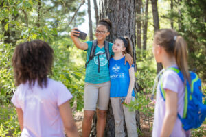 Two girls pose for a selfie in front of a tree.