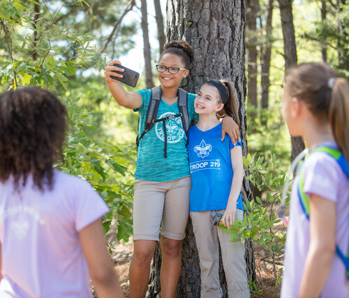 Two girls pose for a selfie in front of a tree.